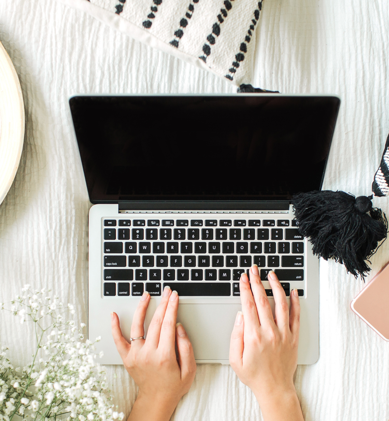 A person typing on a laptop with a blank screen, placed on a white textured surface next to white flowers and a slide4 decorative piece, evoking a serene and productive workspace.